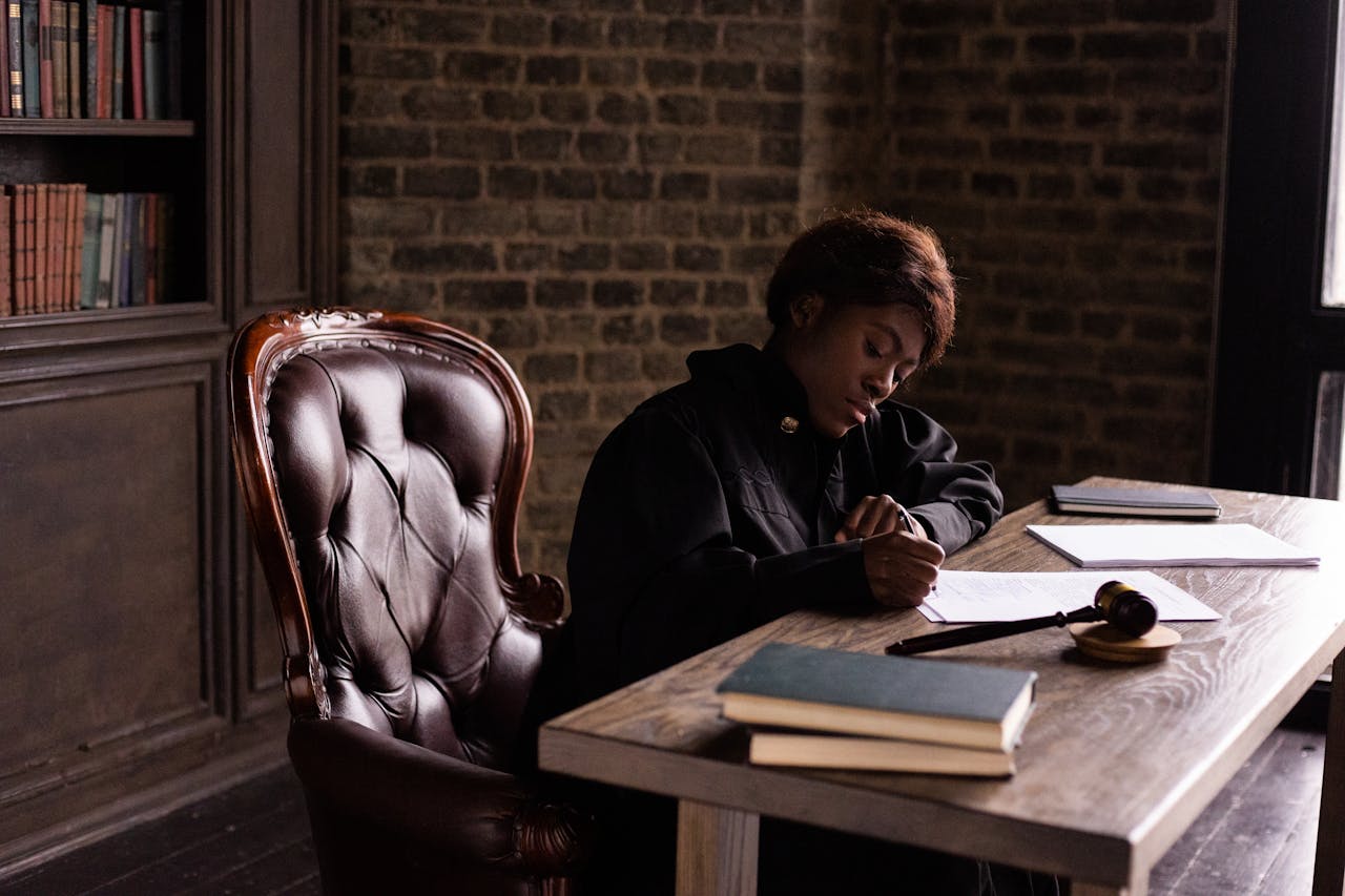 Black female judge in judicial robe writing at desk in an office setting, focusing on legal work.